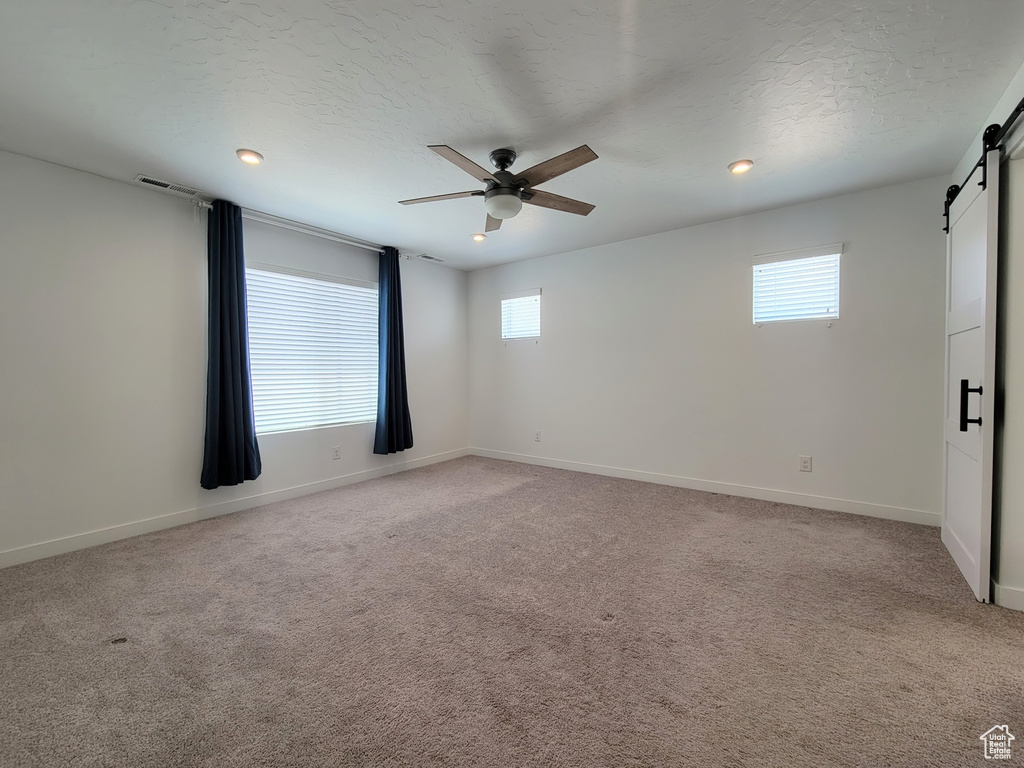 Unfurnished room with a barn door, ceiling fan, plenty of natural light, light carpet, and recessed lighting