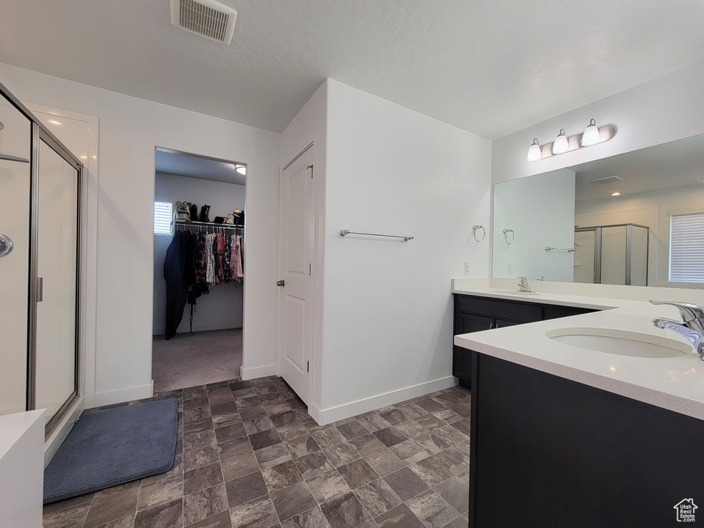 Bathroom with a stall shower, baseboards, vanity, a walk in closet, and stone finish floors