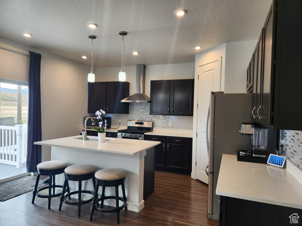 Kitchen featuring wall chimney exhaust hood, stainless steel appliances, a sink, dark wood-type flooring, and tasteful backsplash