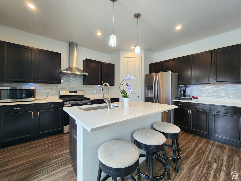 Kitchen featuring wall chimney range hood, appliances with stainless steel finishes, a sink, dark wood-style flooring, and decorative backsplash