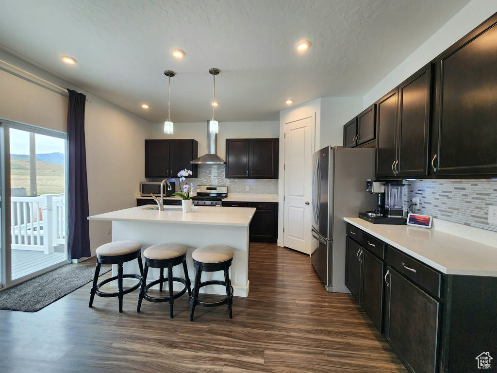 Kitchen featuring stainless steel appliances, backsplash, light countertops, a center island with sink, and recessed lighting