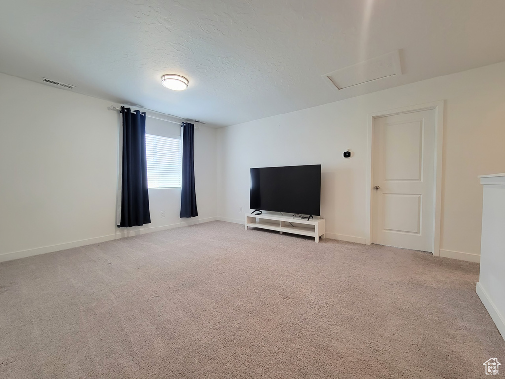 Unfurnished living room featuring baseboards, attic access, and light carpet