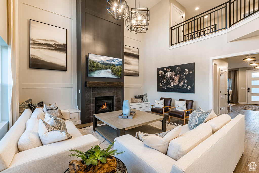 Living room with light wood-type flooring, a fireplace, a towering ceiling, a chandelier, and baseboards