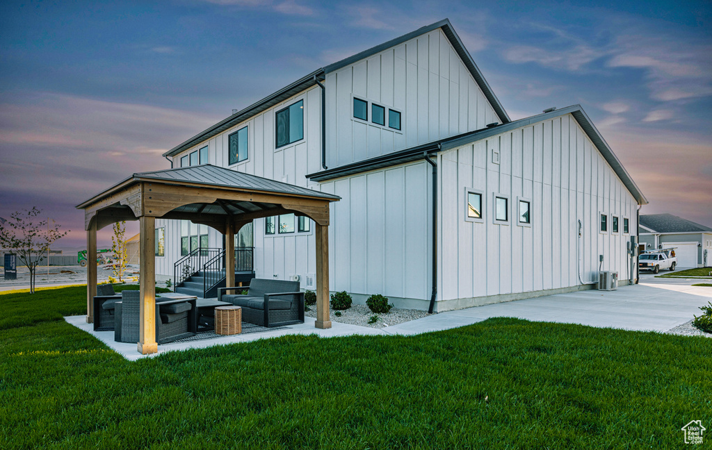 Back of property at dusk featuring a gazebo, board and batten siding, a yard, and cooling unit