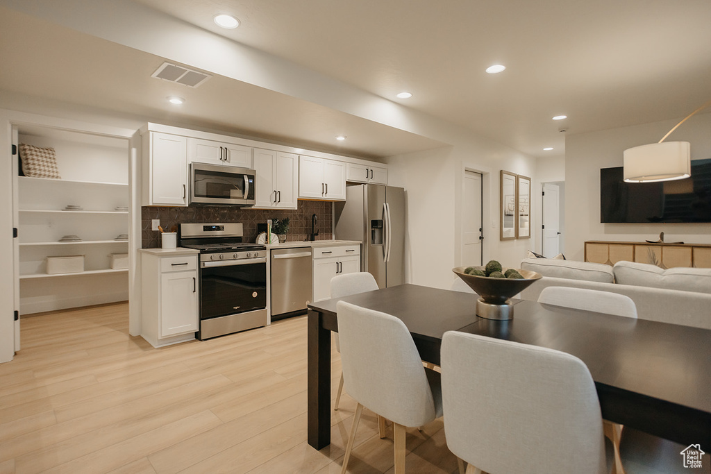 Kitchen with stainless steel appliances, white cabinetry, light wood-type flooring, recessed lighting, and backsplash