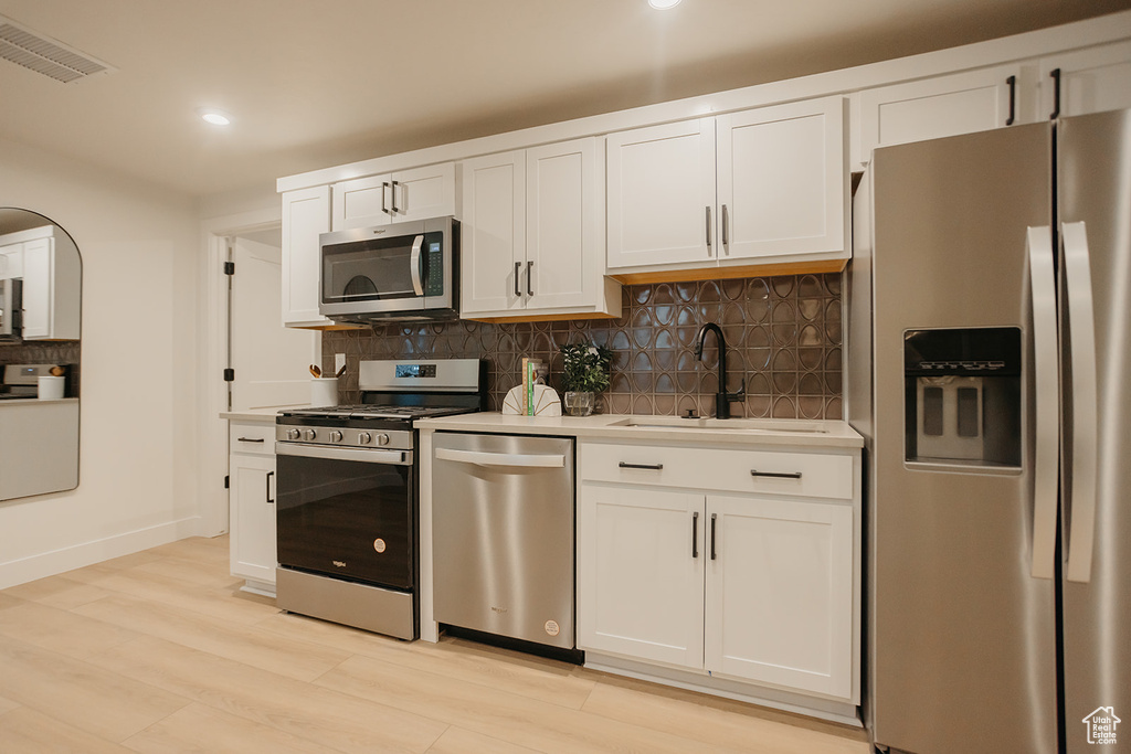 Kitchen with stainless steel appliances, a sink, decorative backsplash, light countertops, and white cabinetry