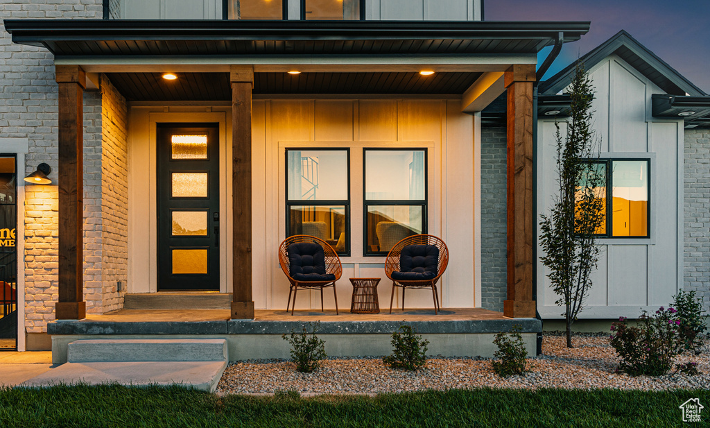 Doorway to property with covered porch, board and batten siding, and brick siding