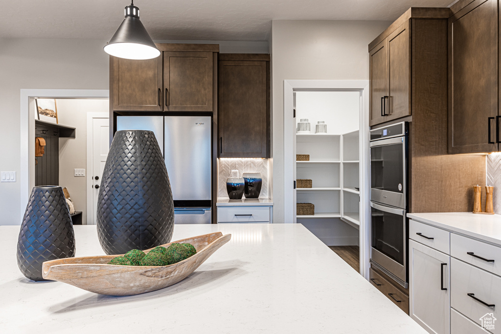 Kitchen with appliances with stainless steel finishes, decorative backsplash, dark brown cabinetry, decorative light fixtures, and light stone counters