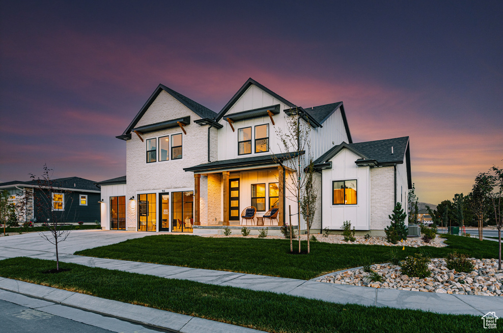 View of front of home with a porch, driveway, board and batten siding, a lawn, and an attached garage