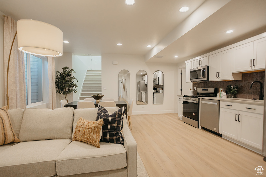 Kitchen featuring appliances with stainless steel finishes, a sink, light wood finished floors, tasteful backsplash, and white cabinetry