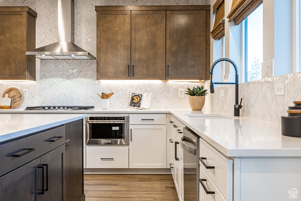 Kitchen featuring wall chimney range hood, a sink, stainless steel appliances, light wood-style floors, and white cabinetry