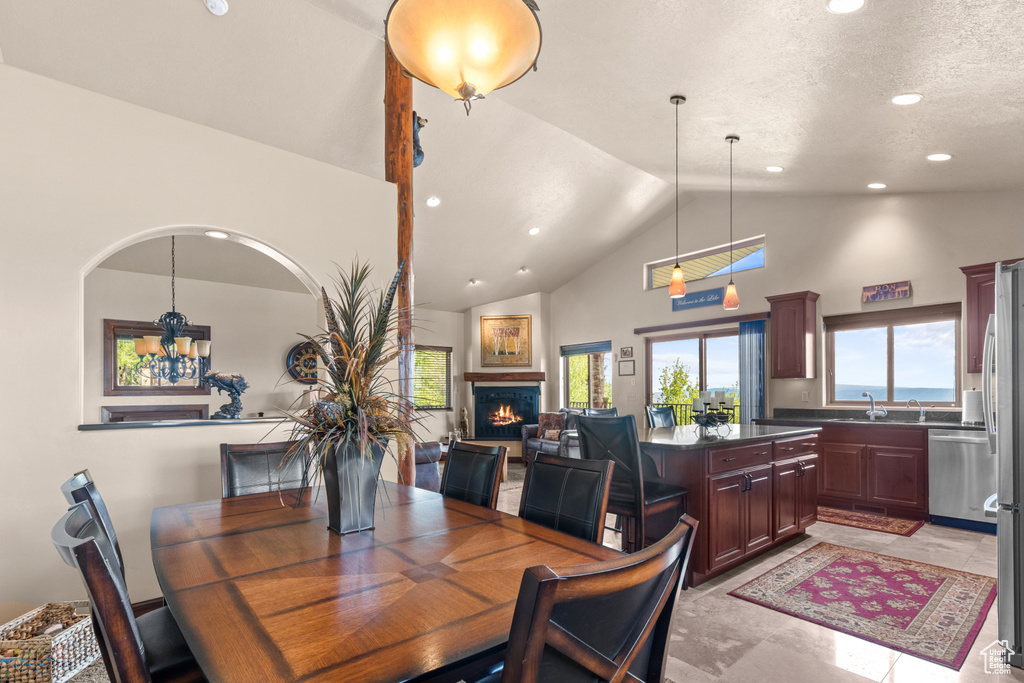 Dining space with a warm lit fireplace, high vaulted ceiling, recessed lighting, and a chandelier