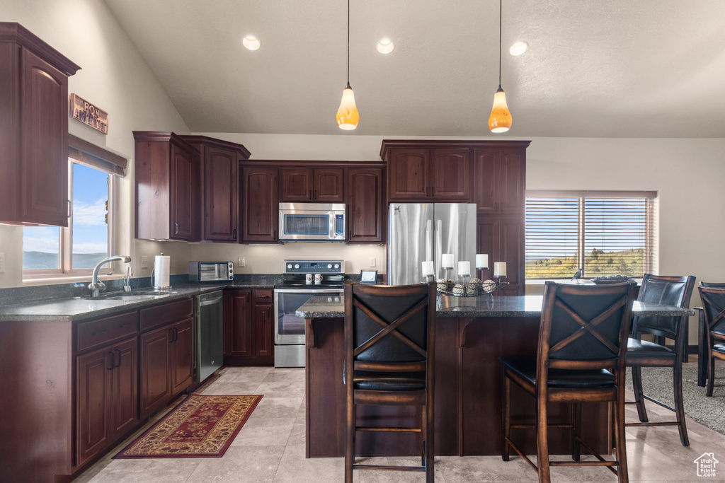 Kitchen with appliances with stainless steel finishes, a sink, lofted ceiling, a center island, and a kitchen bar