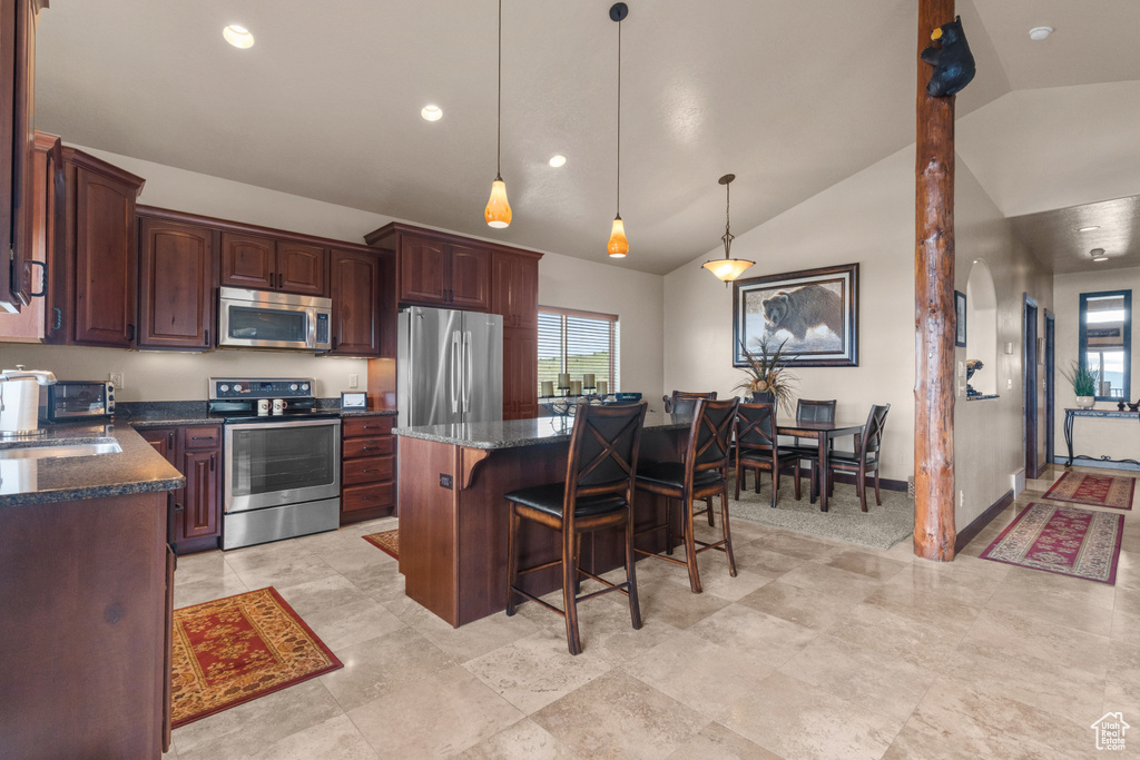 Kitchen featuring stainless steel appliances, a breakfast bar area, a sink, a center island, and dark stone countertops