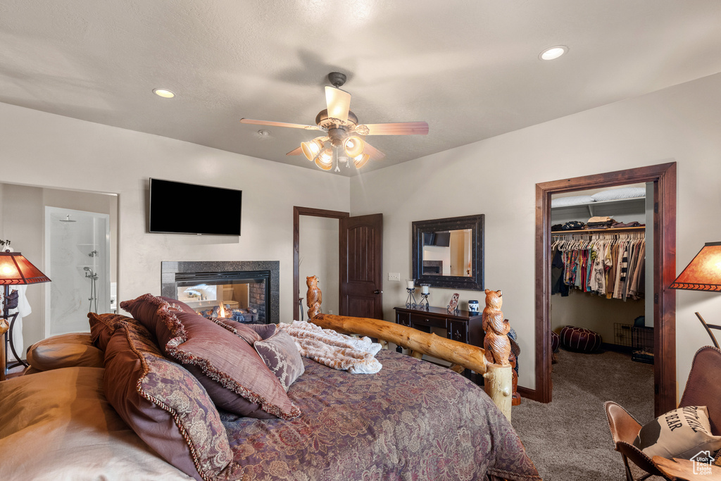 Carpeted bedroom featuring a walk in closet, baseboards, a closet, ceiling fan, and a multi sided fireplace