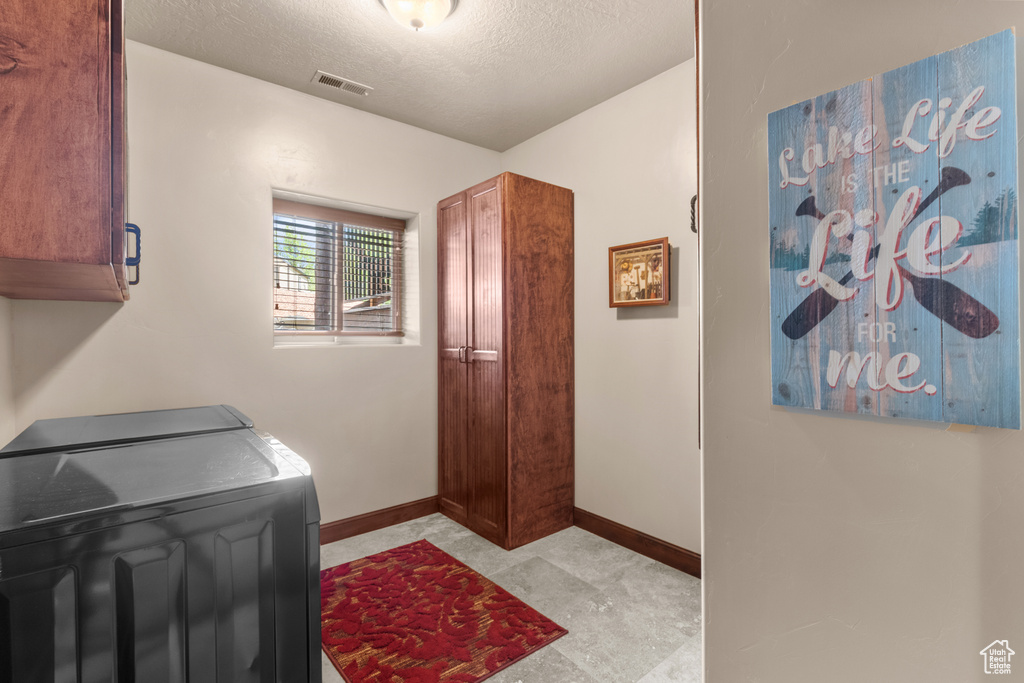 Laundry area featuring cabinet space, washer and clothes dryer, a textured ceiling, and baseboards