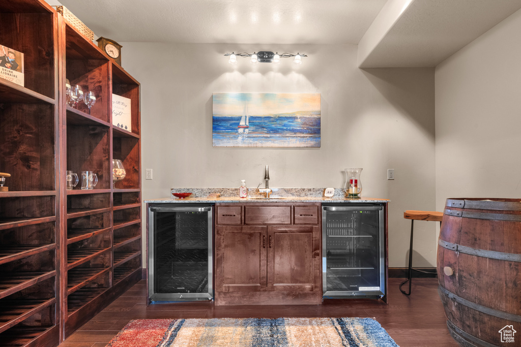 Indoor wet bar with wine cooler, dark wood-type flooring, and baseboards
