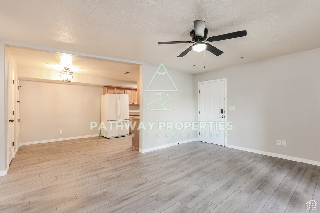 Spare room with light wood-style flooring, ceiling fan, baseboards, and a textured ceiling