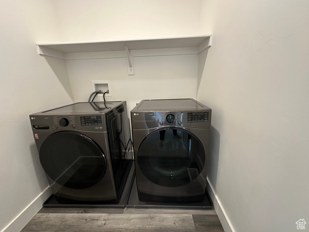 Clothes washing area featuring washing machine and dryer, wood finished floors, and baseboards