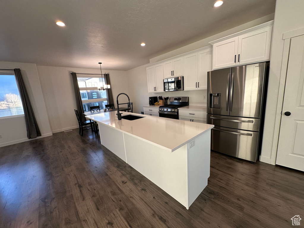 Kitchen featuring appliances with stainless steel finishes, a sink, a kitchen island with sink, dark wood-type flooring, and white cabinetry
