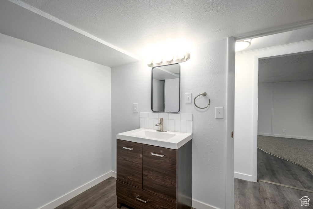 Bathroom featuring wood finished floors, vanity, baseboards, backsplash, and a textured ceiling