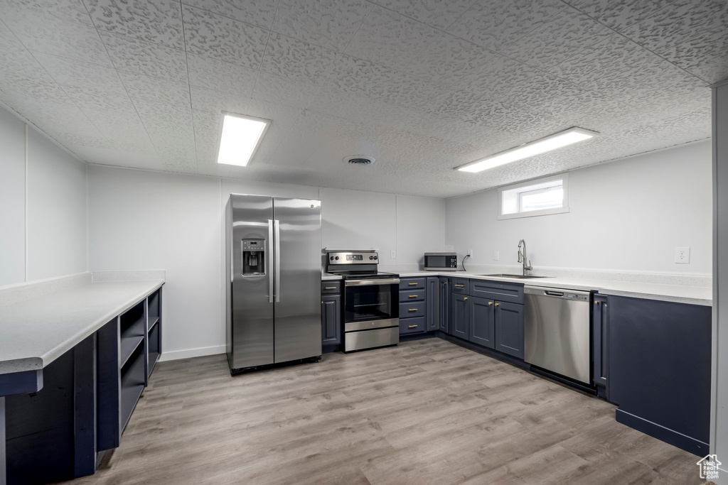 Kitchen with stainless steel appliances, a sink, blue cabinetry, and light wood-style floors
