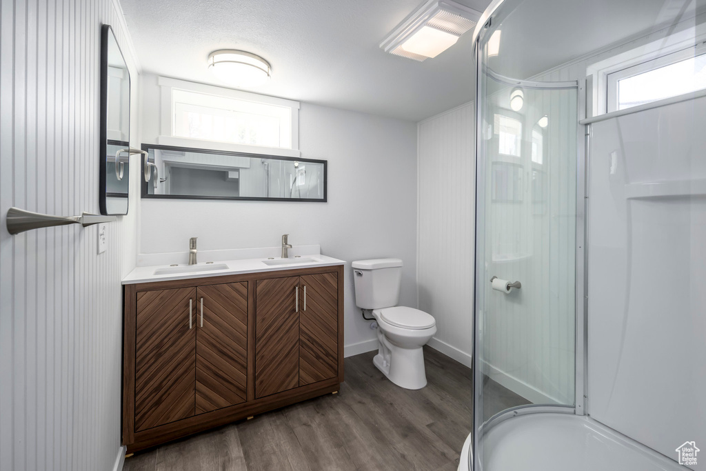 Full bath featuring a shower stall, wood finished floors, toilet, double vanity, and plenty of natural light