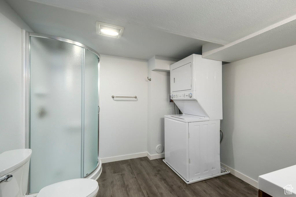 Full bathroom featuring stacked washer / drying machine, wood finished floors, toilet, a stall shower, and a textured ceiling