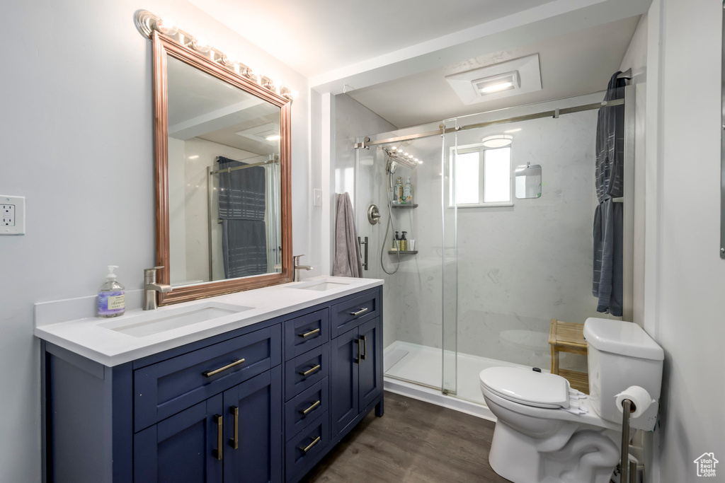 Full bath with toilet, a marble finish shower, double vanity, and wood finished floors