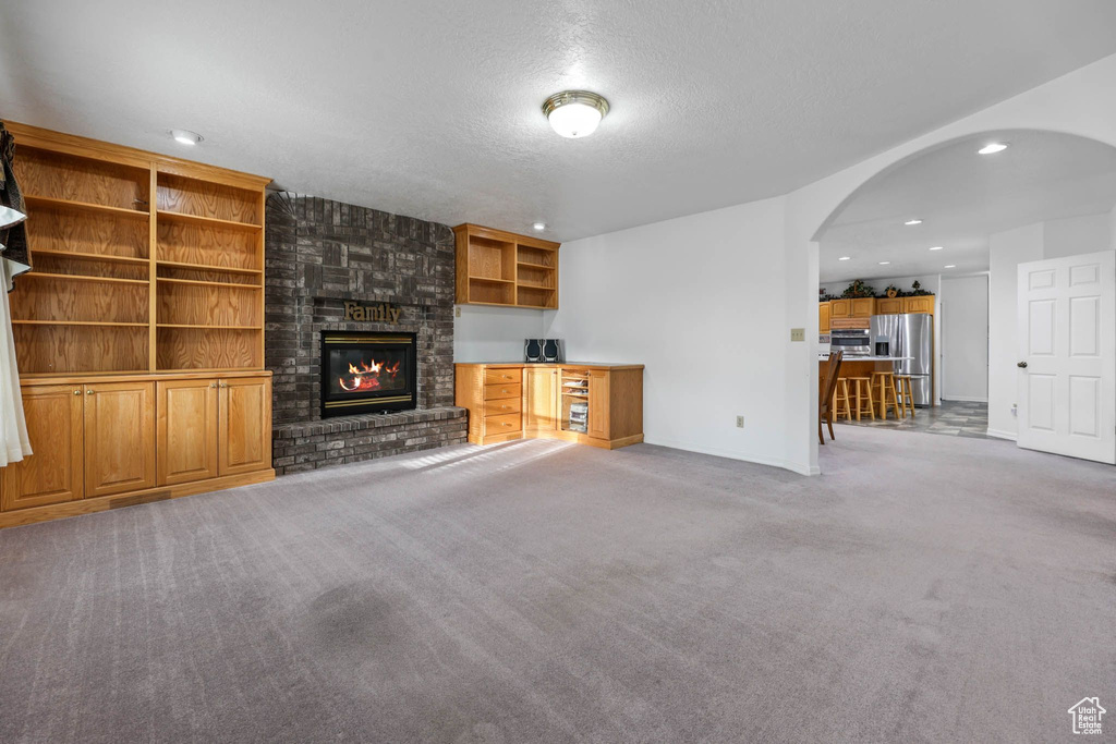 Unfurnished living room with arched walkways, carpet, a brick fireplace, a textured ceiling, and recessed lighting