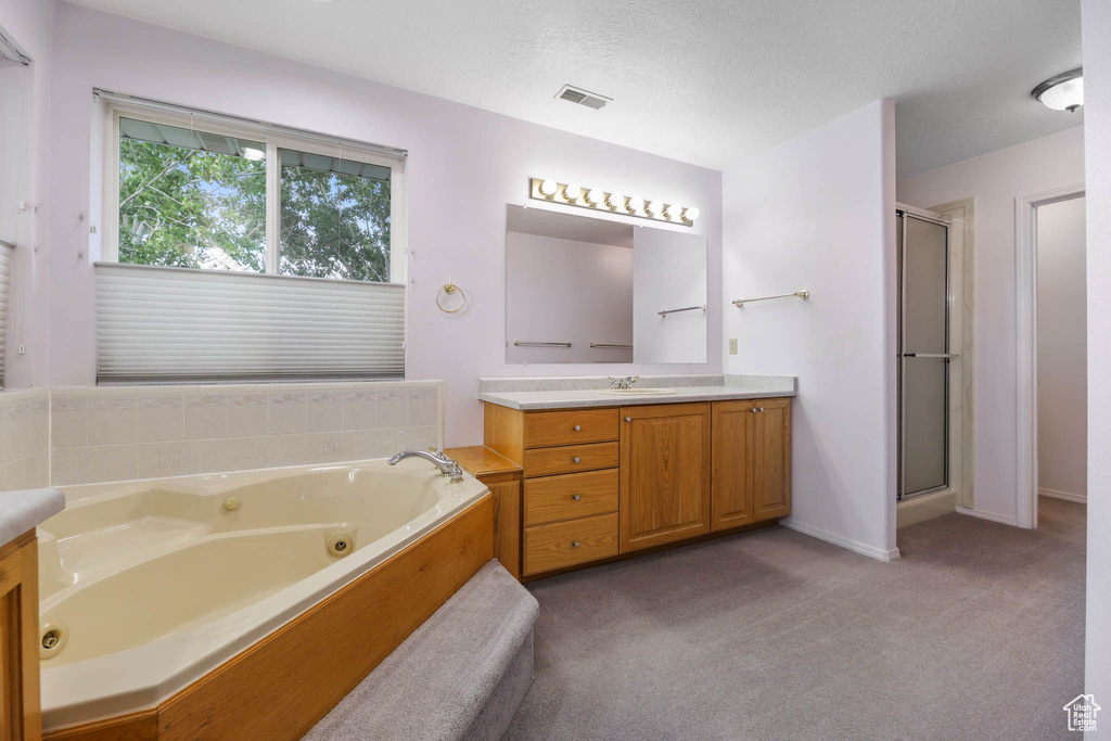 Full bath with vanity, a stall shower, a tub with jets, a textured ceiling, and baseboards