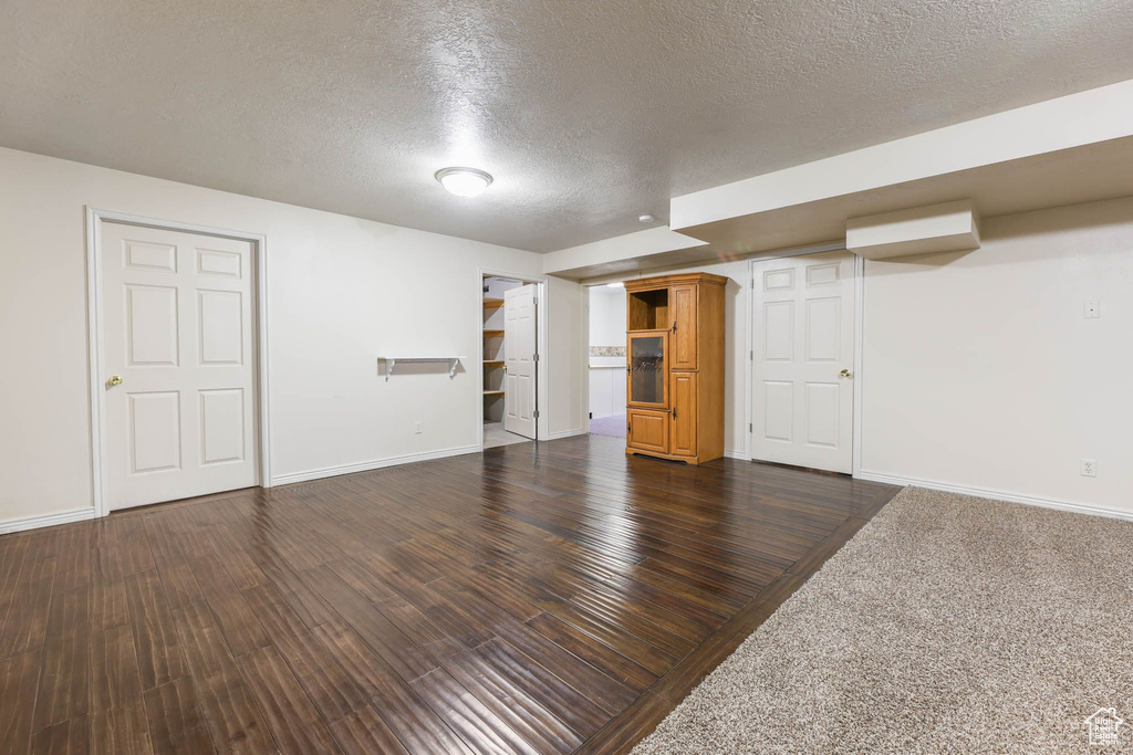Finished basement featuring a textured ceiling, baseboards, and dark wood finished floors