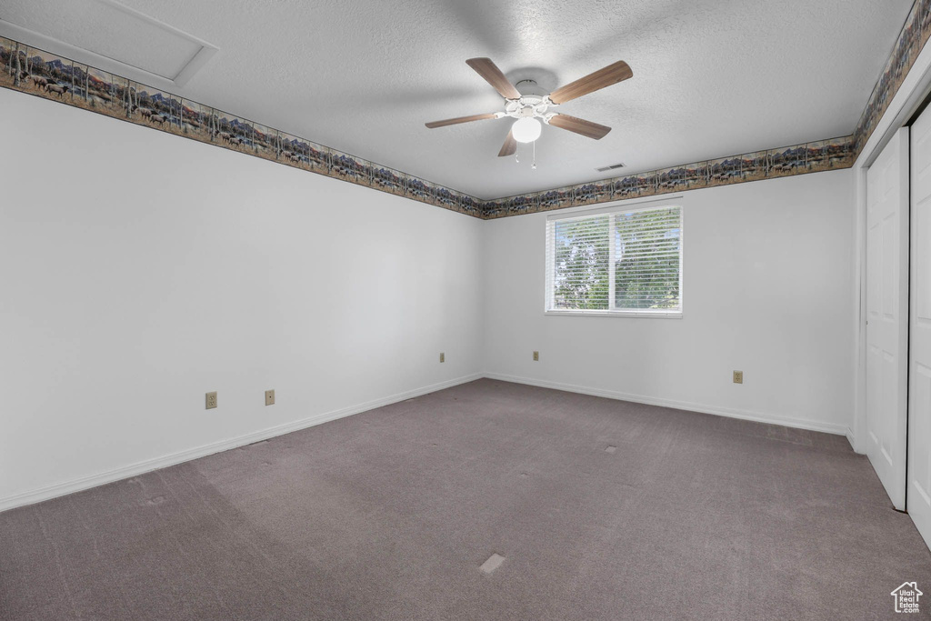 Carpeted empty room with a textured ceiling, ceiling fan, and baseboards
