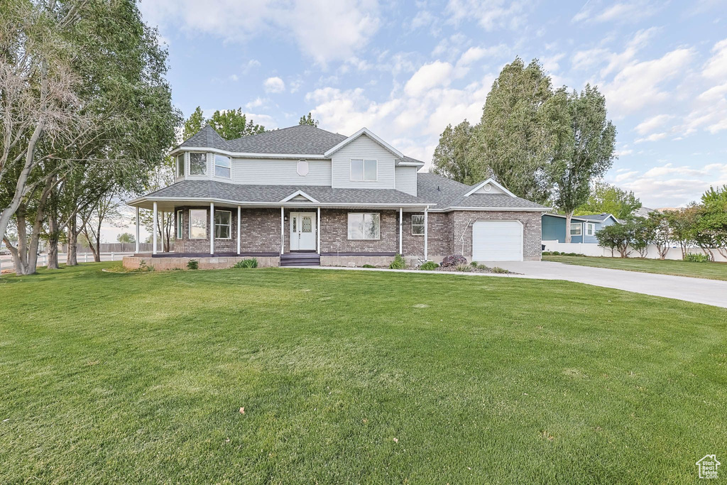 View of front of property with concrete driveway, a front lawn, a garage, a porch, and a shingled roof