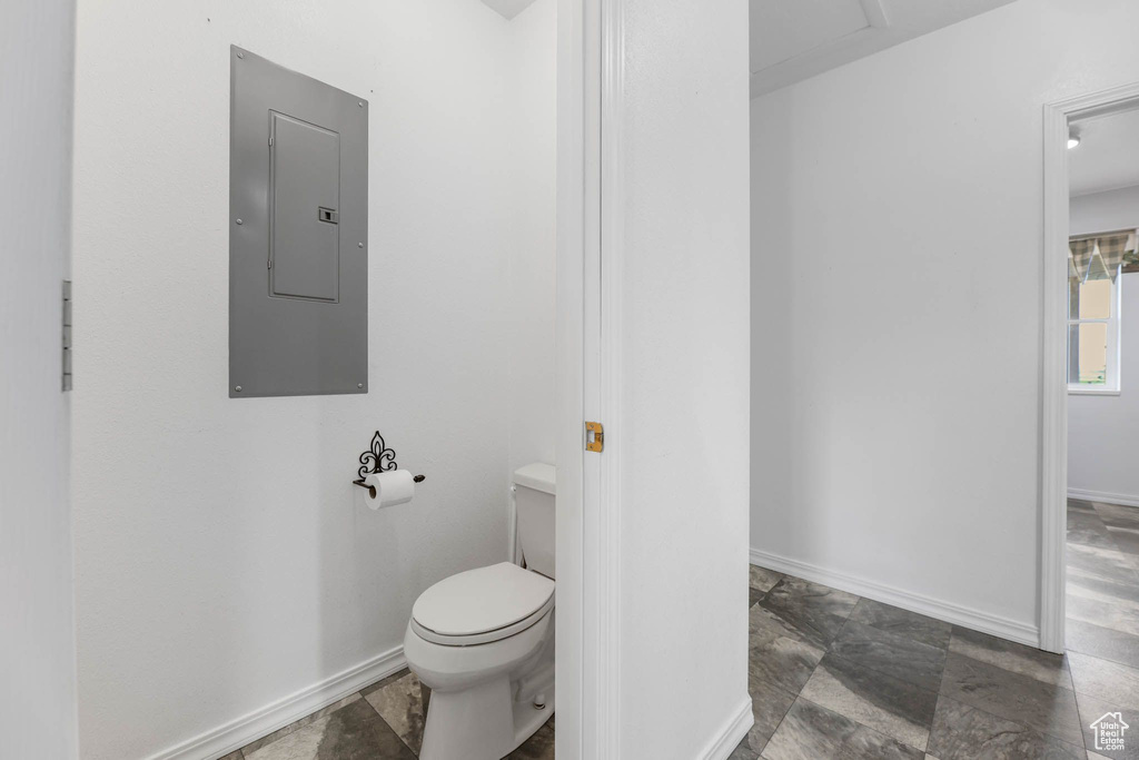 Bathroom with electric panel, toilet, stone finish floors, and baseboards