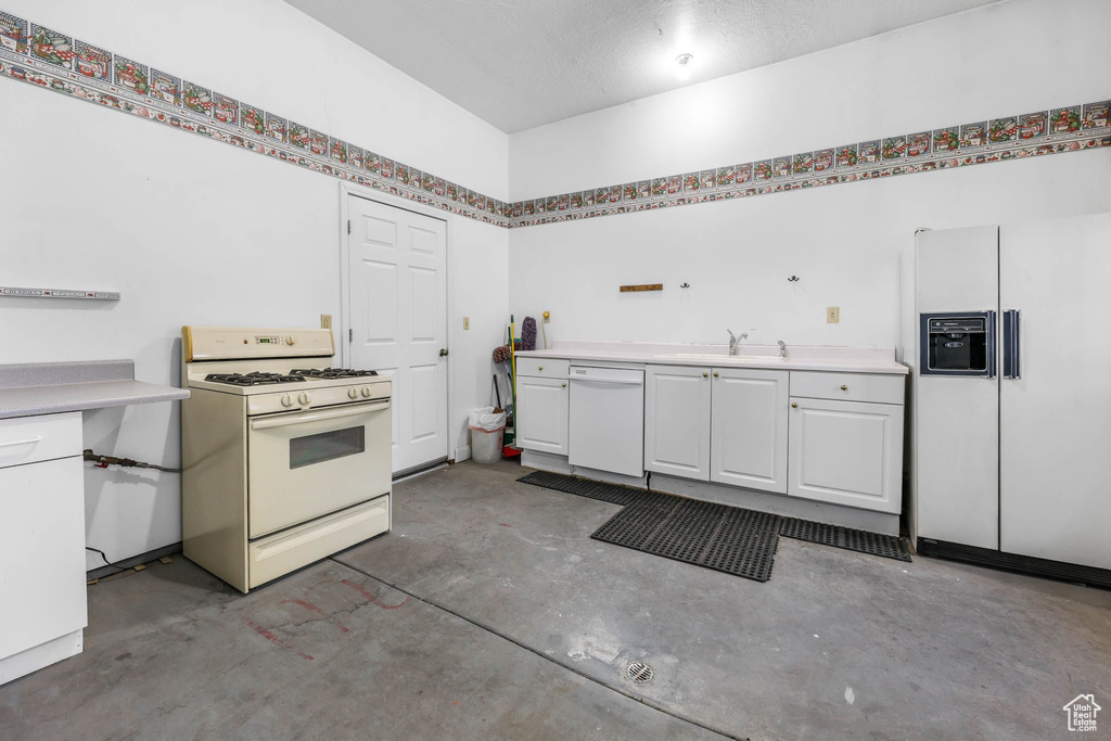 Kitchen with white appliances, concrete floors, white cabinets, light countertops, and a sink