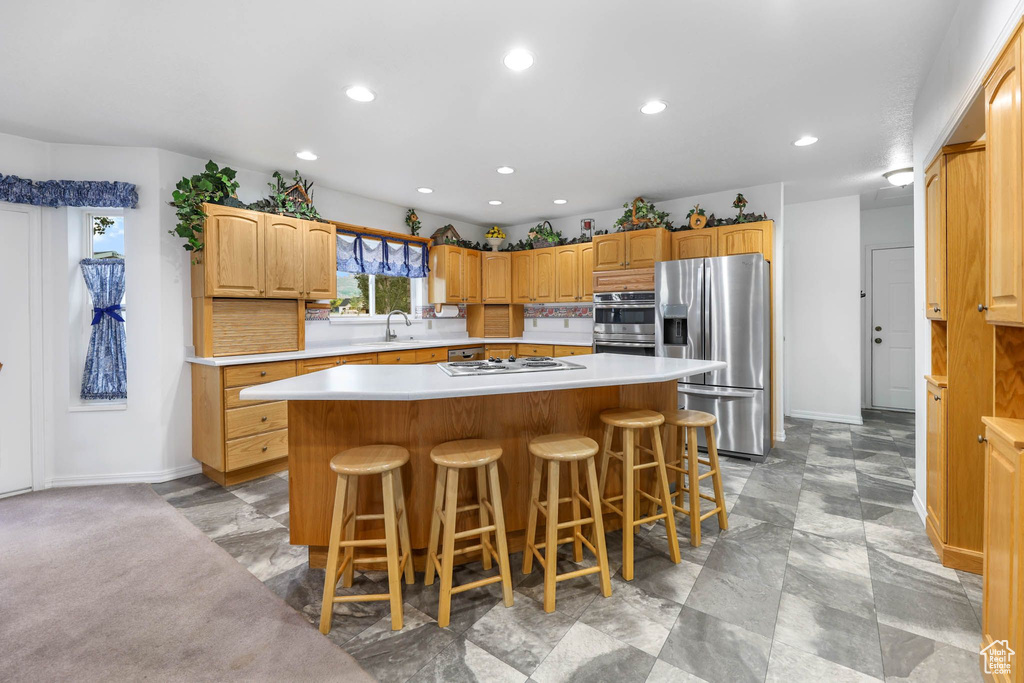 Kitchen featuring stainless steel refrigerator with ice dispenser, a kitchen island, a sink, light countertops, and baseboards