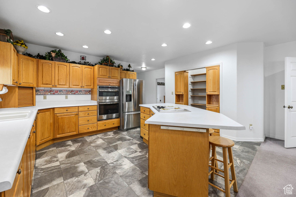 Kitchen featuring appliances with stainless steel finishes, a center island, a sink, recessed lighting, and a kitchen bar