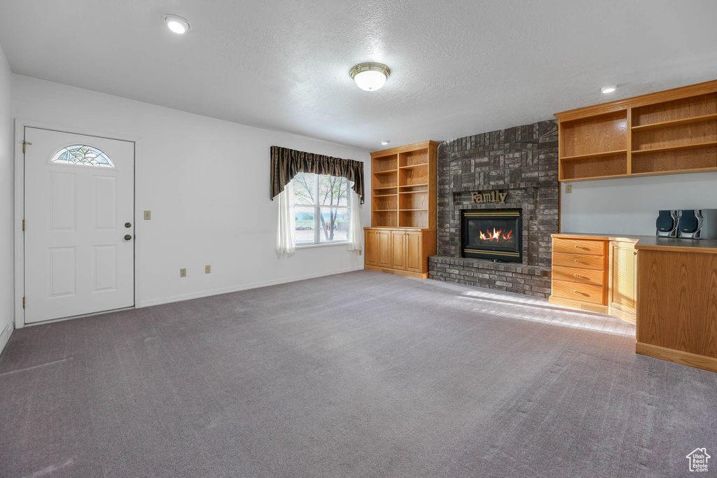 Unfurnished living room featuring a textured ceiling, carpet floors, a fireplace, baseboards, and built in shelves