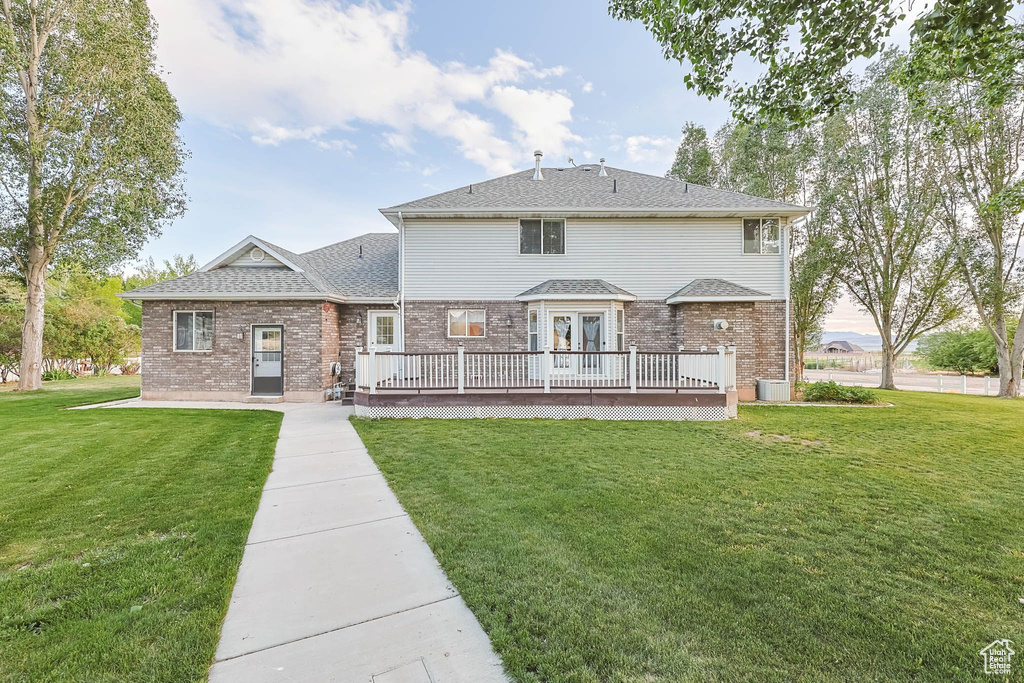 Back of house with a wooden deck, a lawn, brick siding, and cooling unit