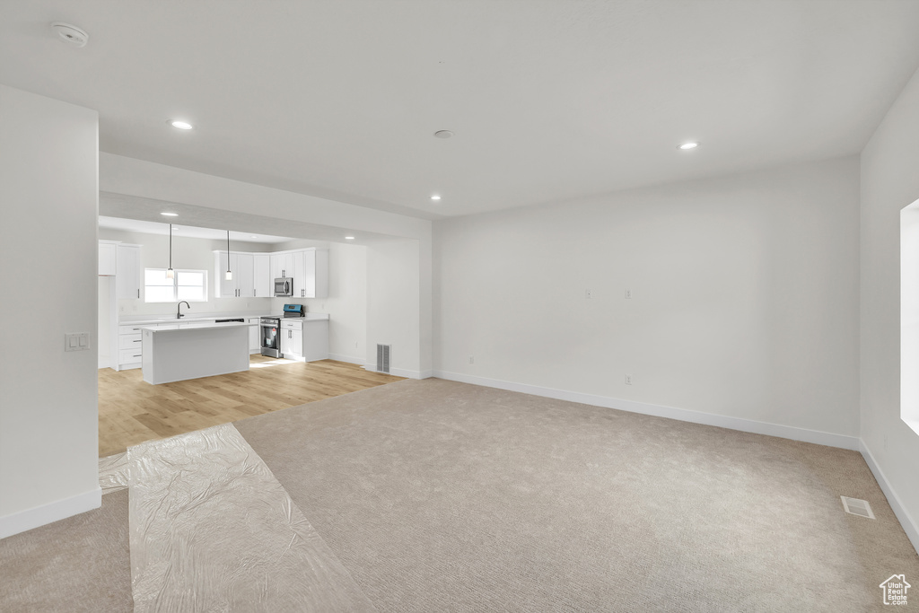 Unfurnished living room with light colored carpet, baseboards, a sink, recessed lighting, and light wood-style flooring