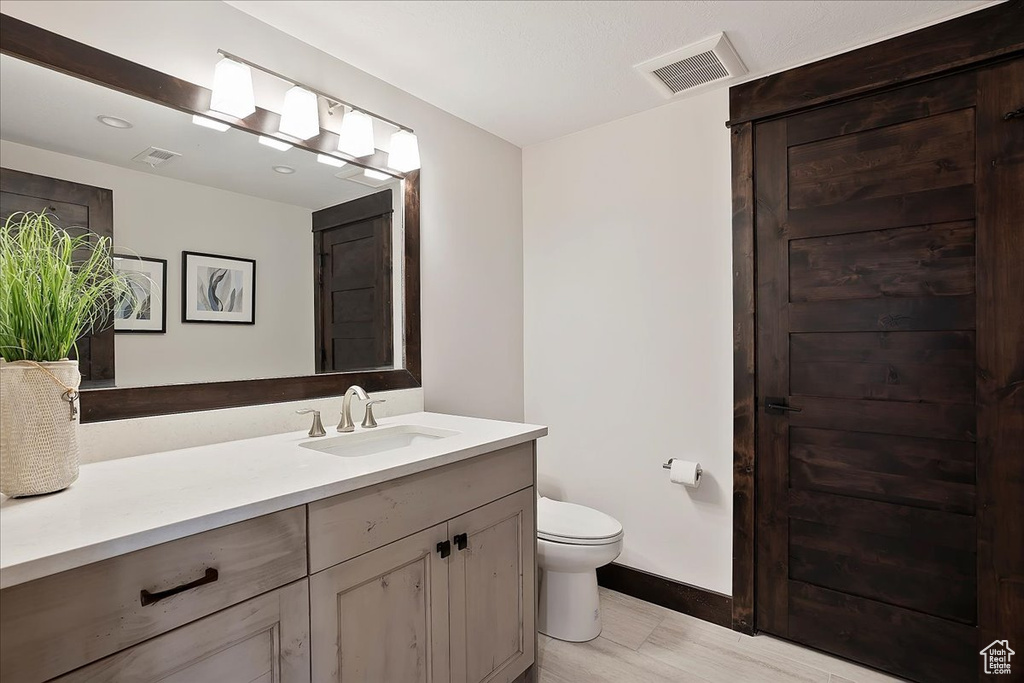 Full bathroom with toilet, vanity, baseboards, and wood finished floors