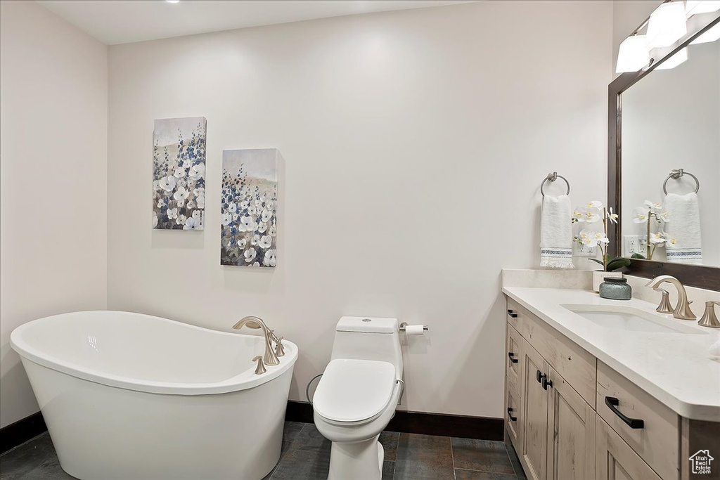 Full bath with baseboards, vanity, a freestanding bath, and toilet