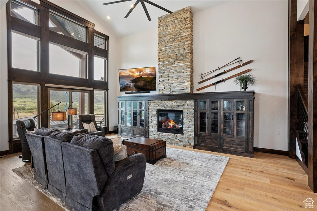 Living area with wood finished floors, baseboards, high vaulted ceiling, a stone fireplace, and a ceiling fan