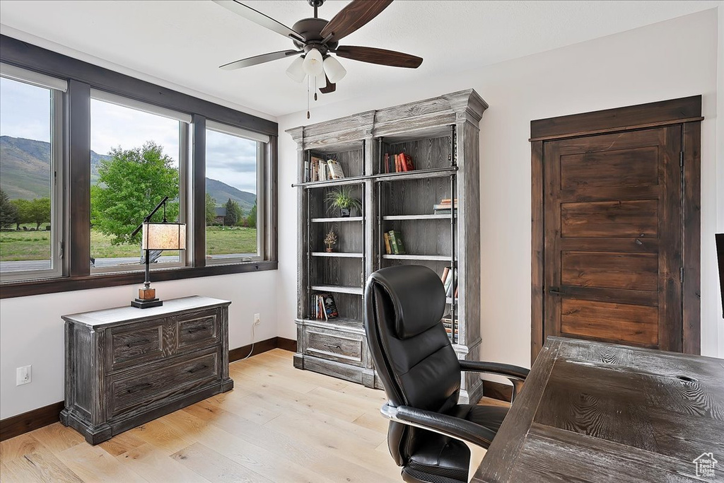 Office space featuring a ceiling fan, baseboards, light wood finished floors, and a mountain view