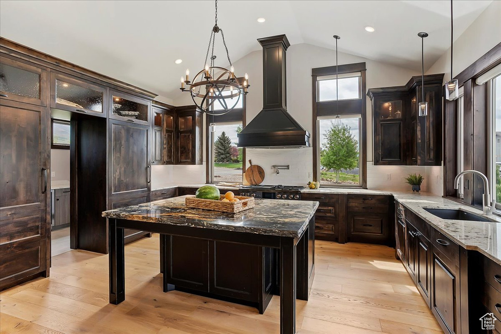 Kitchen featuring a sink, custom range hood, lofted ceiling, plenty of natural light, and dark stone counters