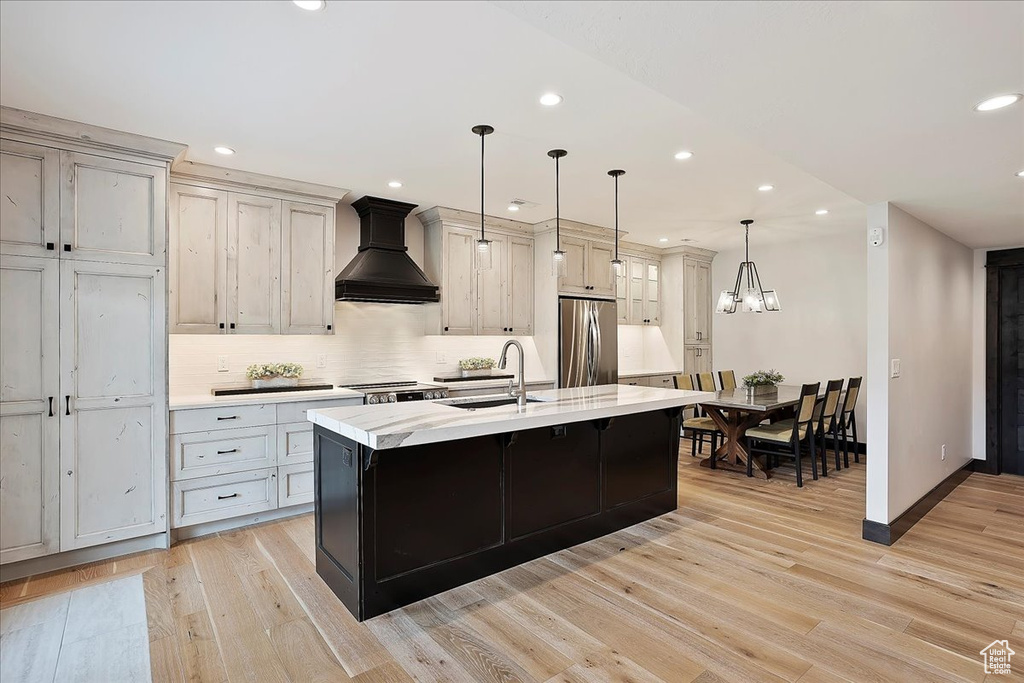 Kitchen with a sink, freestanding refrigerator, custom exhaust hood, recessed lighting, and light wood finished floors