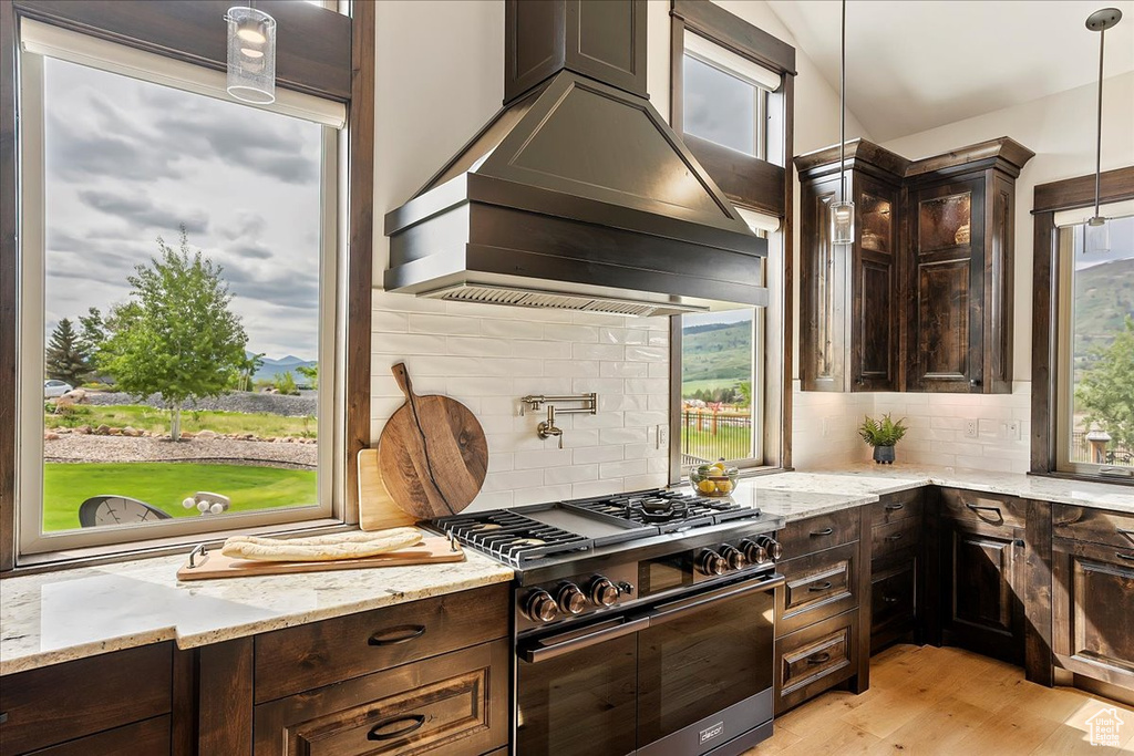 Kitchen with stainless steel range, custom exhaust hood, dark brown cabinetry, decorative backsplash, and lofted ceiling