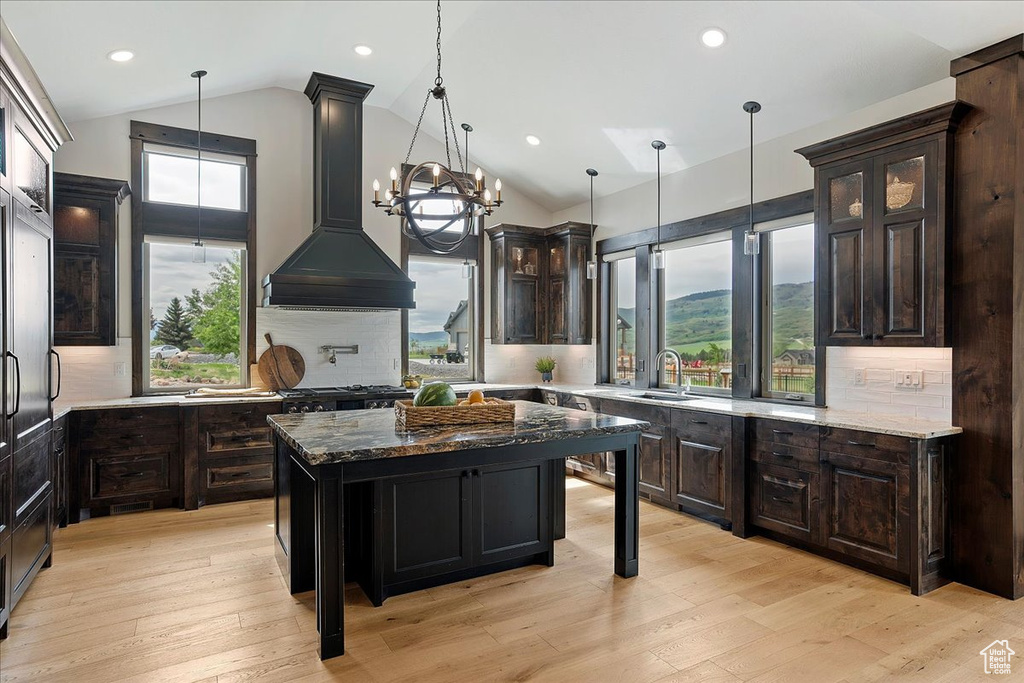 Kitchen featuring a sink, lofted ceiling, custom range hood, dark stone counters, and glass insert cabinets