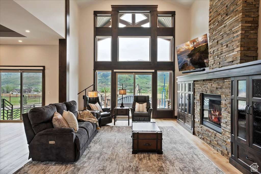 Living area with wood finished floors, a stone fireplace, a high ceiling, and recessed lighting